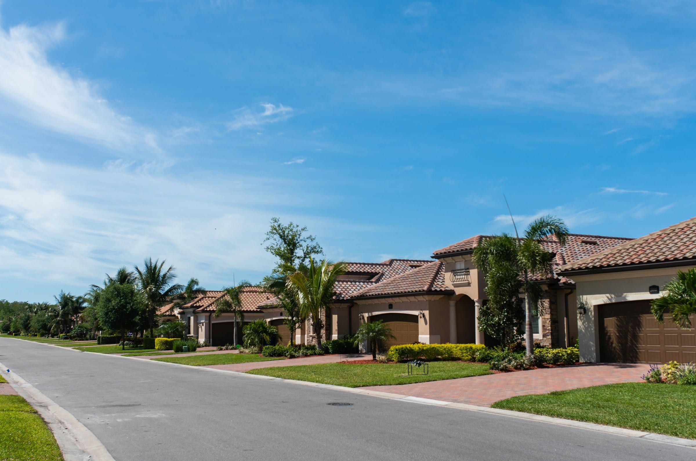 Florida homes with tile roofs, palm trees and paver driveways on a quiet suburban street