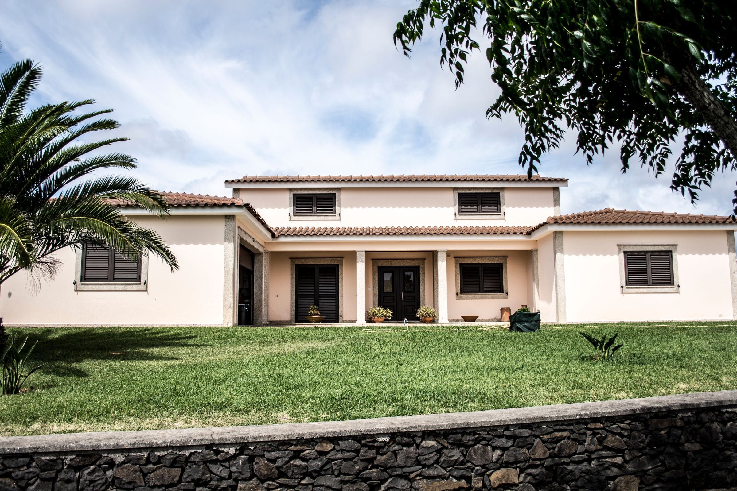 Two-story white stucco home with a tile roof, a covered entry and a palm tree on the front lawn