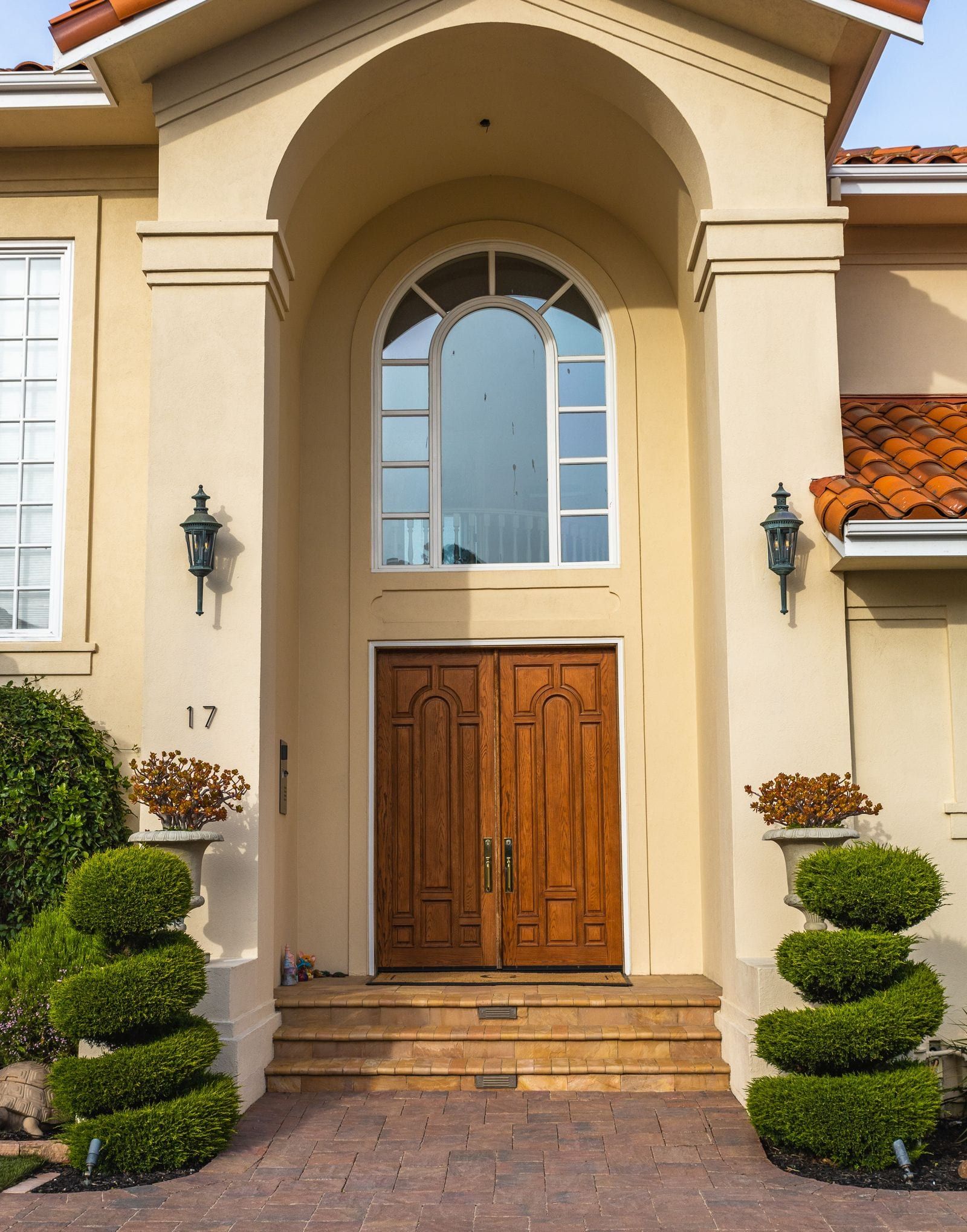 Covered front entry with an arched window, wooden double doors and topiaries