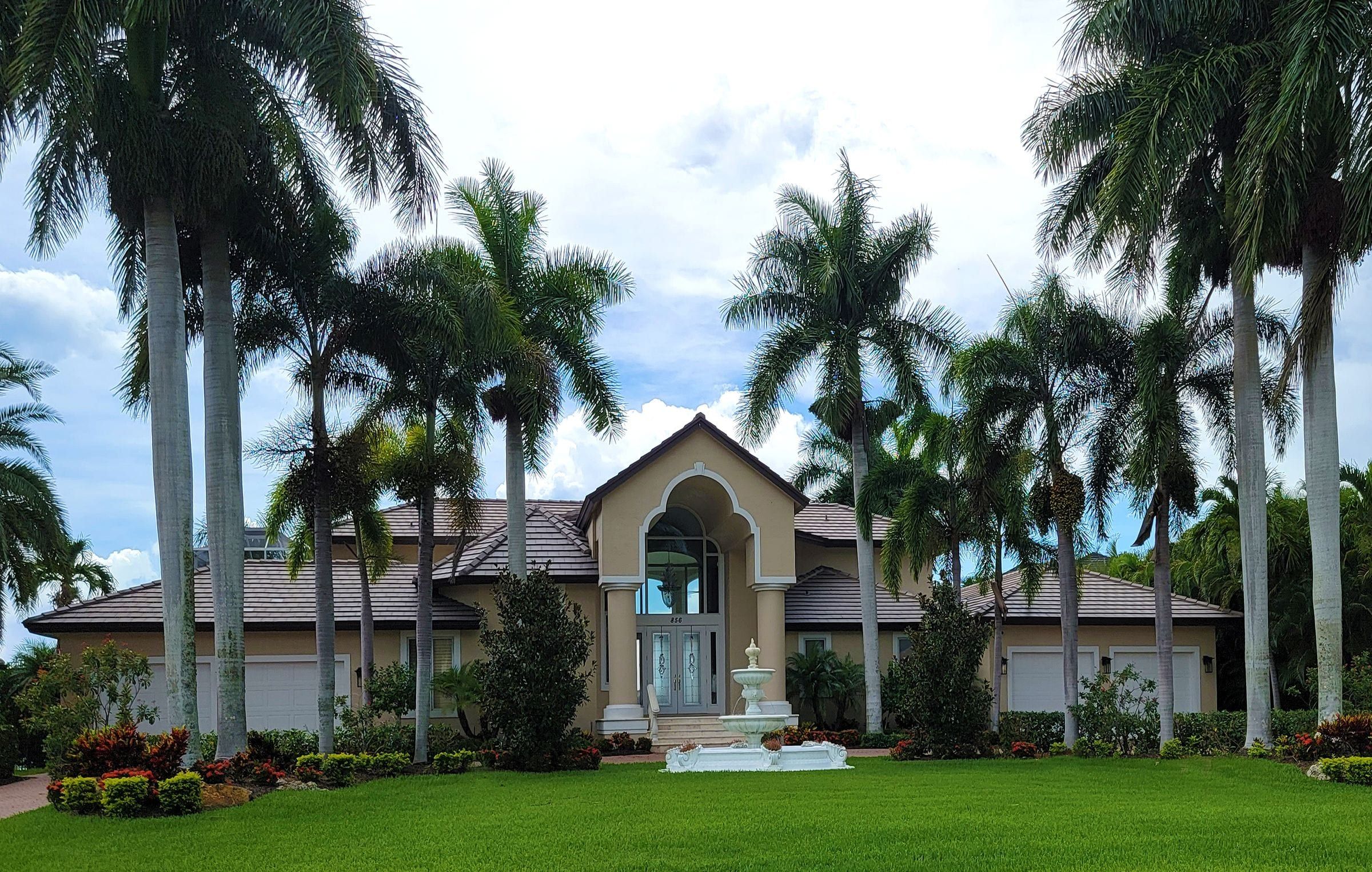 Single-story Florida home with a tile roof, an arched entry and royal palms on a wide lawn