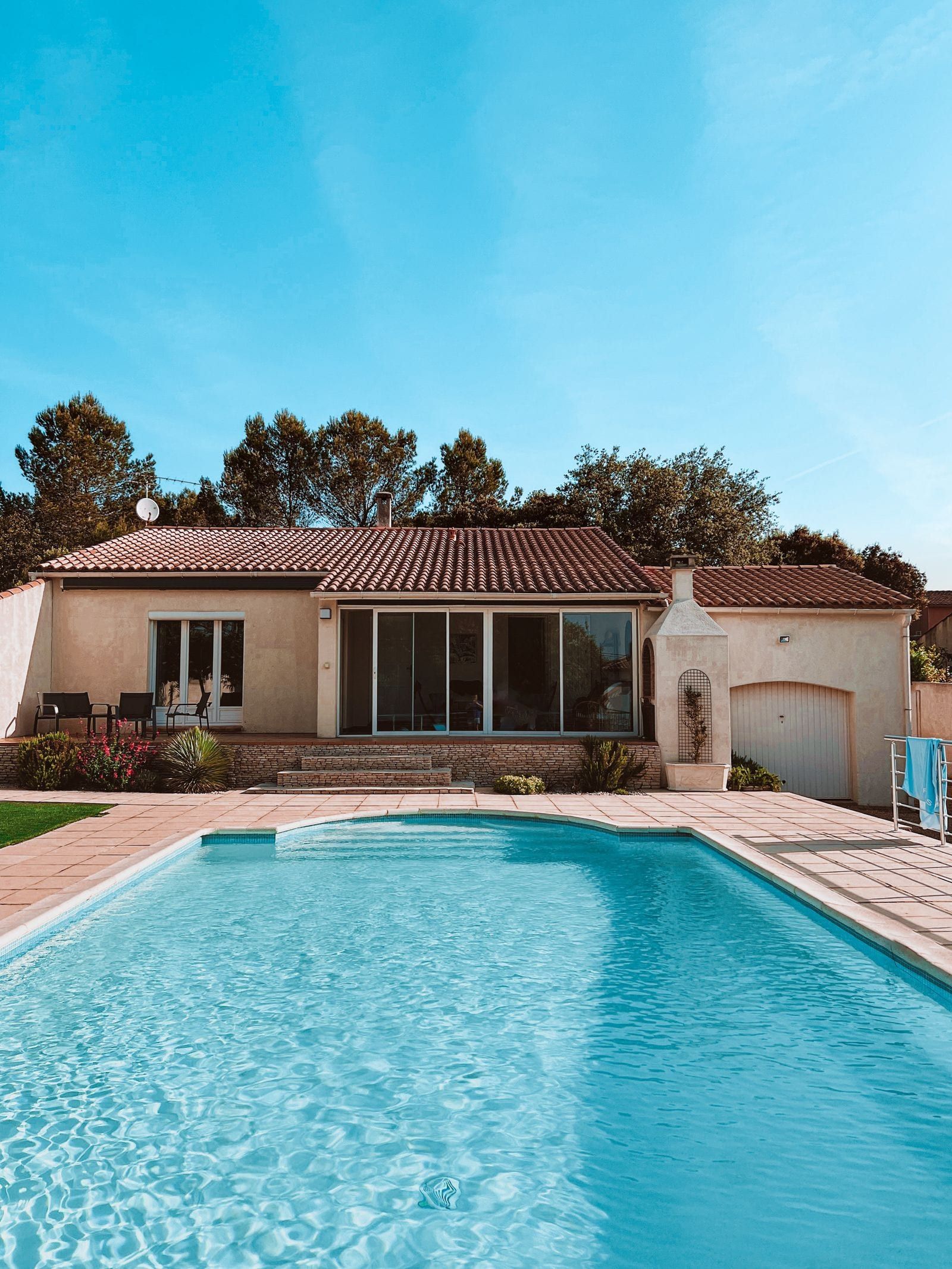 Single-story home with a barrel tile roof behind a rectangular pool with a paver deck