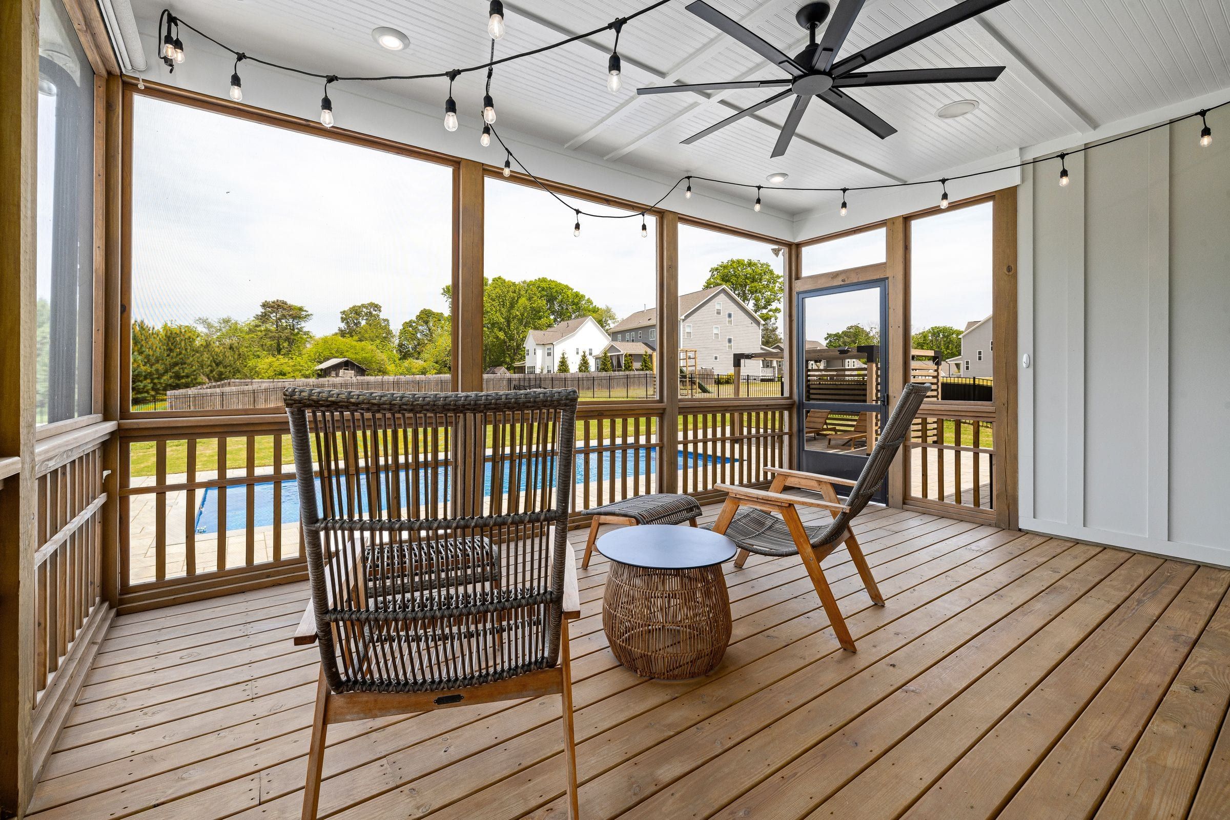 Screened porch with a ceiling fan and seating overlooking the backyard pool