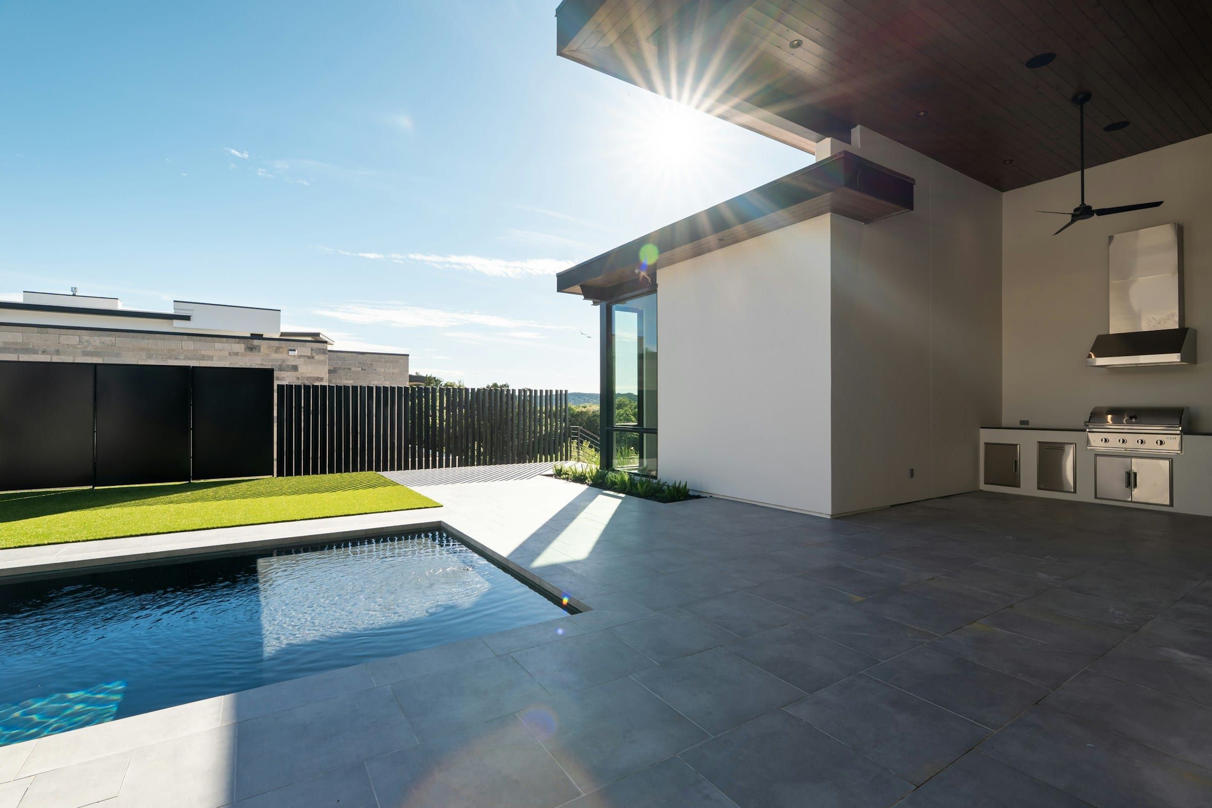 Outdoor kitchen with a built-in grill under a covered patio next to a rectangular pool