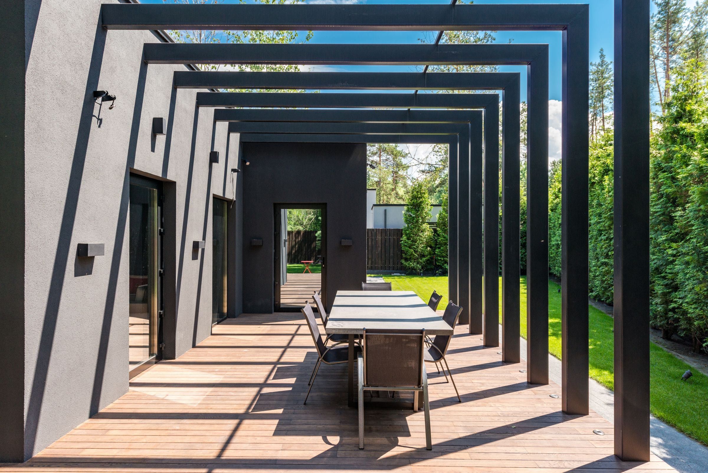 Black steel pergola over an outdoor dining table on a wood deck