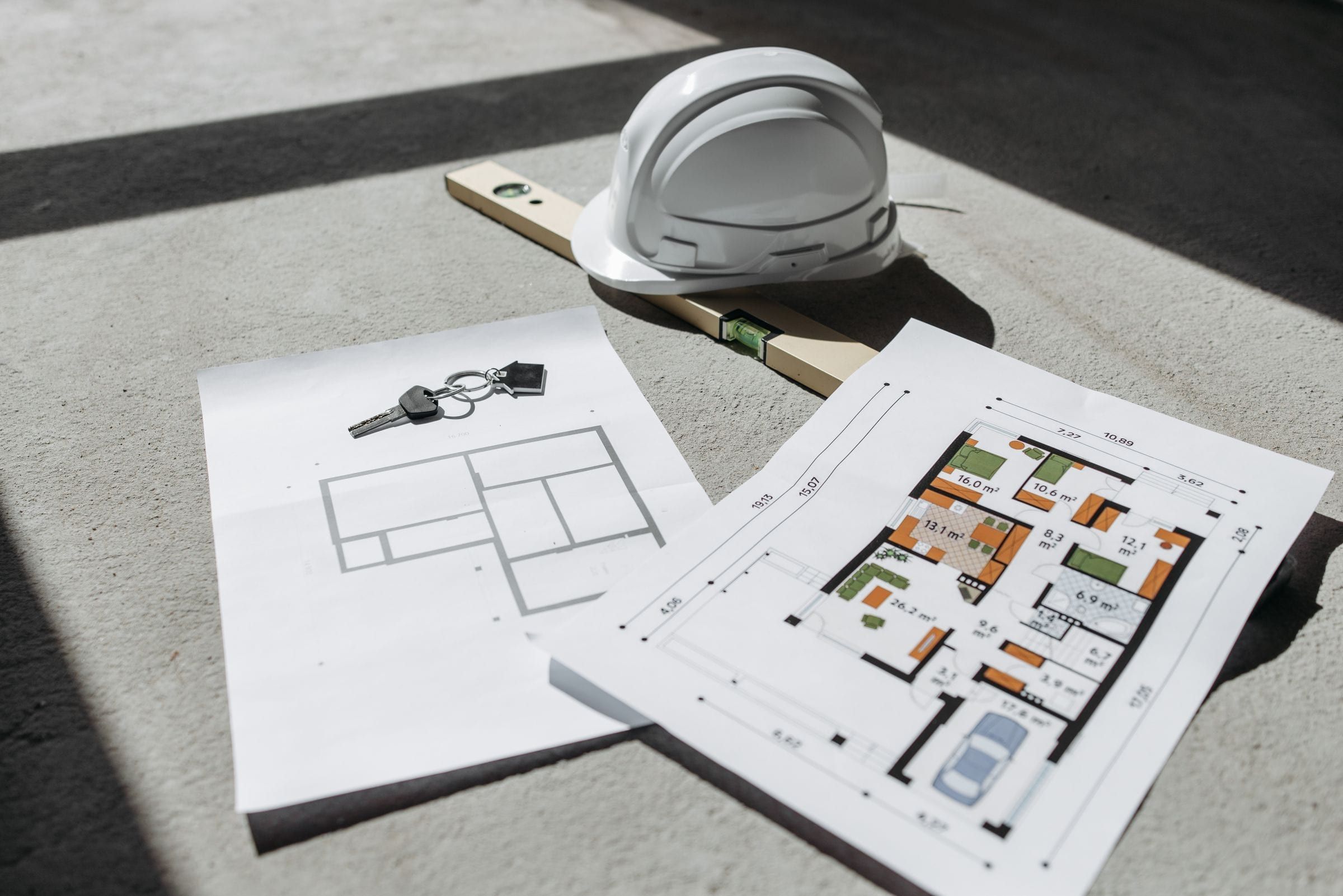 House plans on a slab with a hard hat, a level and a set of keys