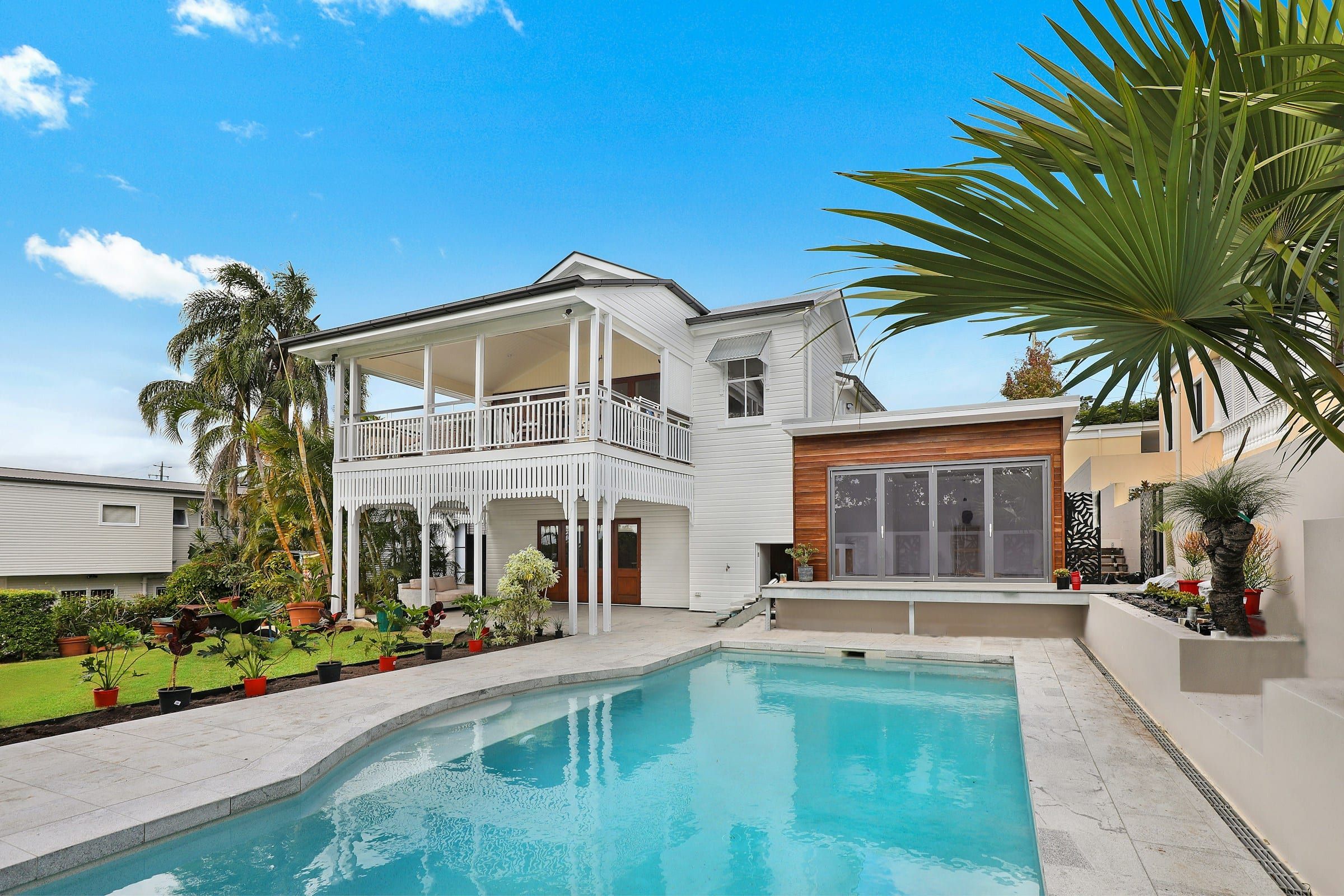 Backyard pool with a travertine deck and palm trees behind a white two-story home