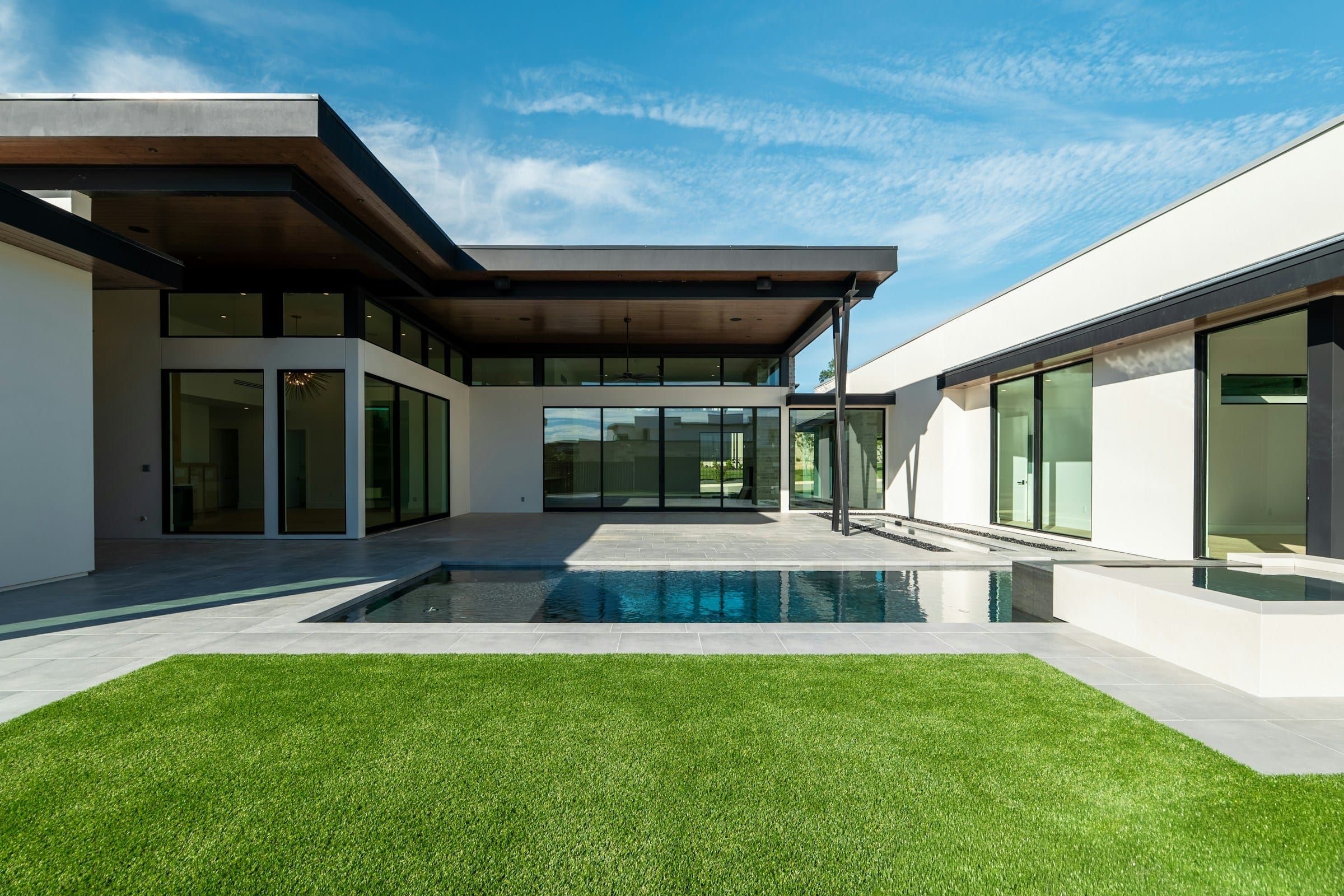 Modern single-story home with a rectangular pool, a porcelain deck and a lawn