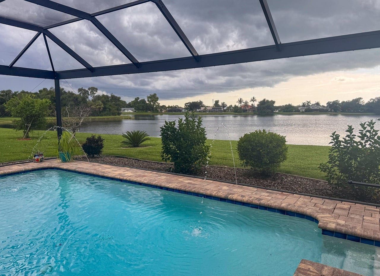 Renovated pool with deck jets and a brick paver deck inside a screen enclosure facing a lake