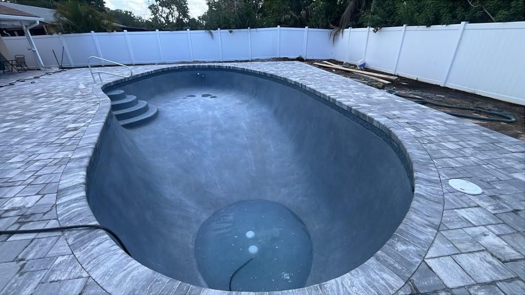 Drained pool with a new dark gray interior finish and new paver coping and deck, before refilling