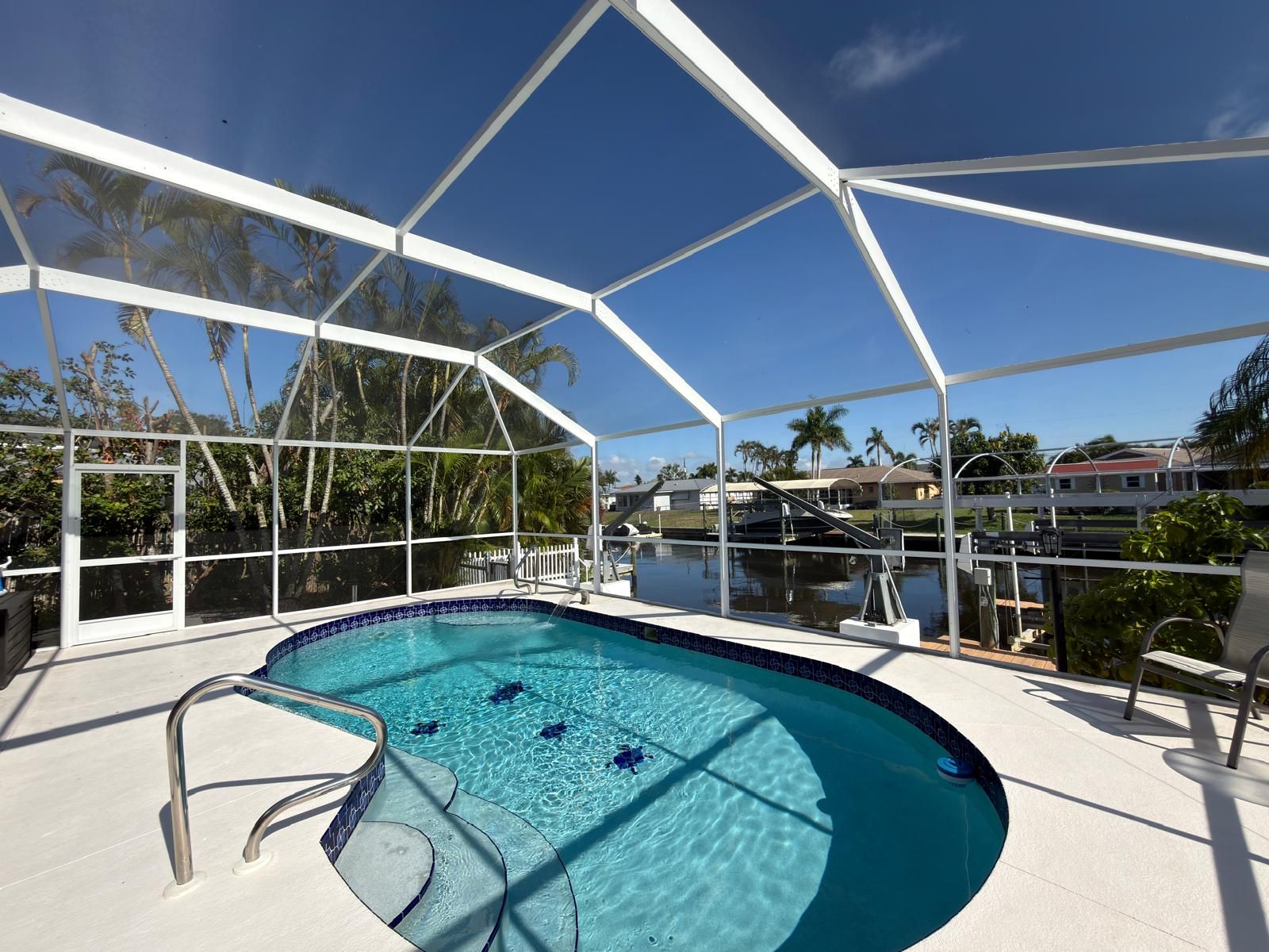 Pool under a white screen enclosure with a light deck, a handrail at the steps and a view of the canal and docks