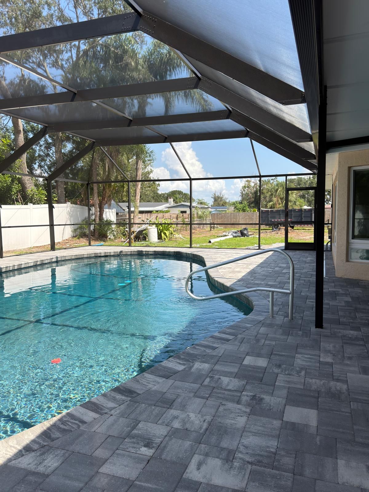 Bronze screen enclosure over a freeform pool with a gray paver deck, next to the back of the house