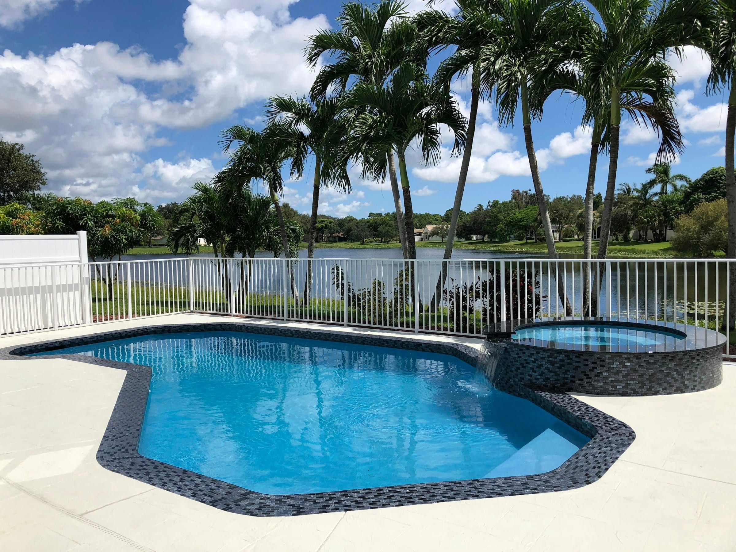 Raised spa with mosaic tile beside a pool, with palm trees and a lake behind