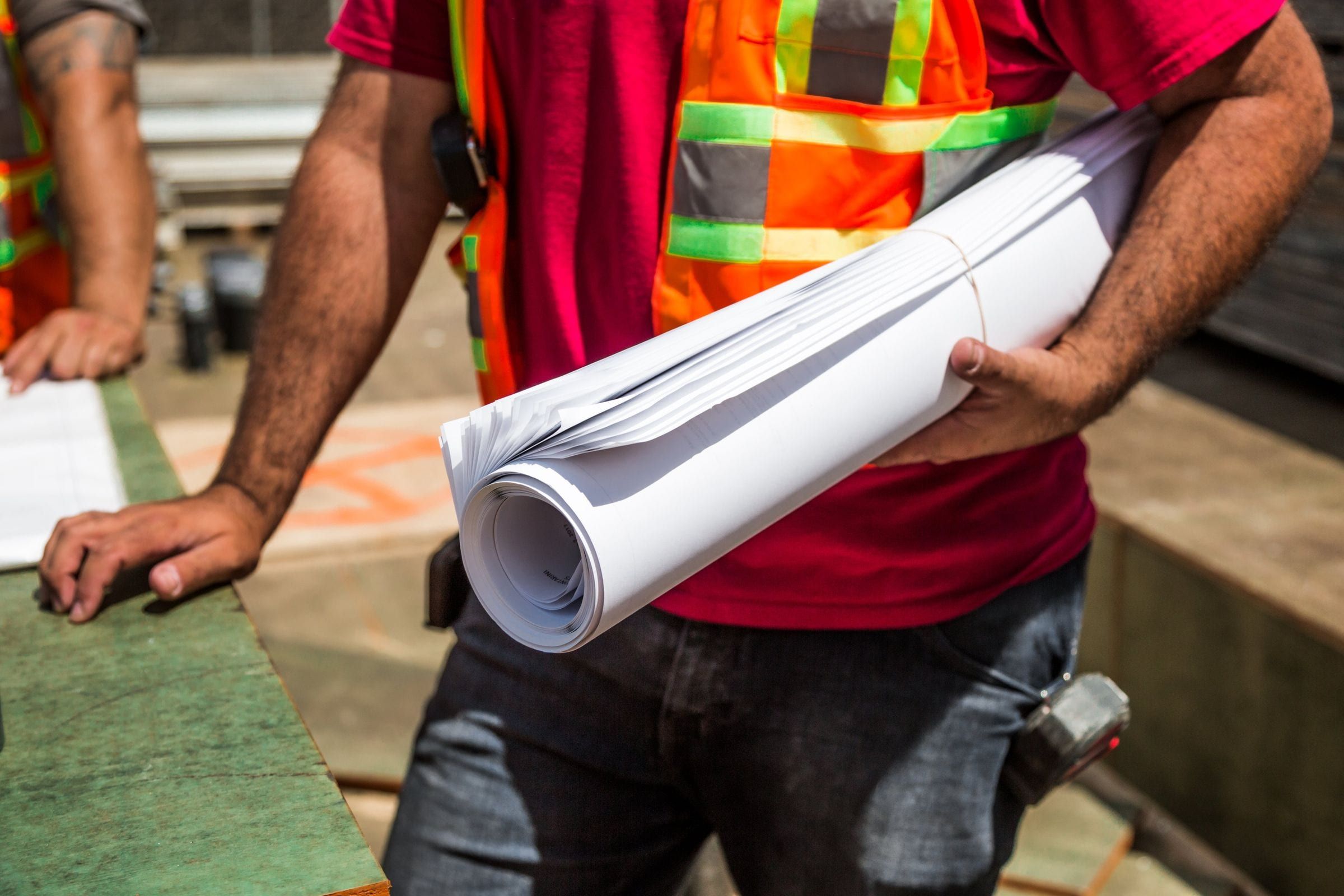 Builder in a safety vest carrying a roll of house plans on a job site